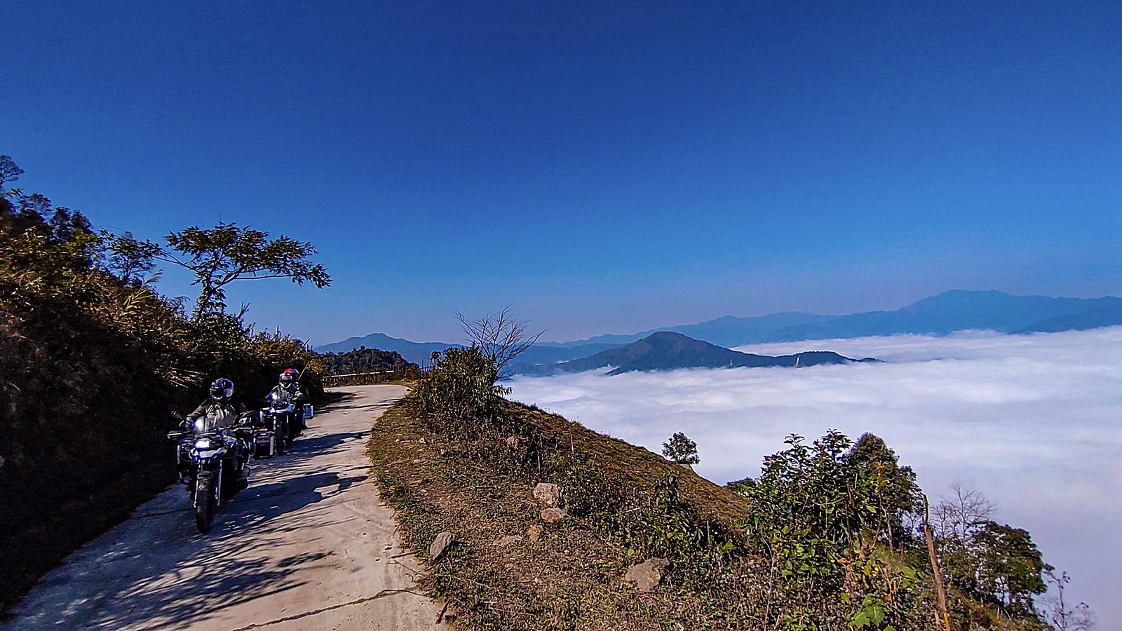 Hai xe mô tô chạy trên con đường ven sườn núi, biển mây trắng phía dưới